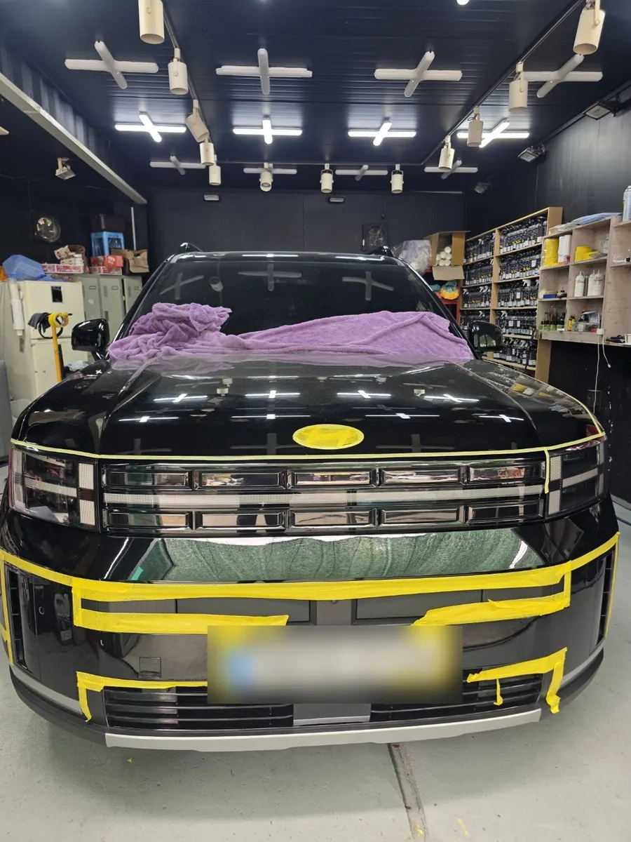 검은색 SUV 앞범퍼와 번호판 둘레, 그릴 경계에 노란 마스킹 테이프를 붙인 모습. 넘버원세차장 실내 작업장